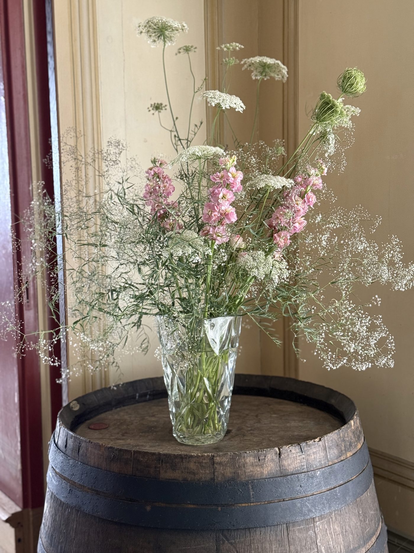 Zarte Sommerblumen in Glasvase auf Weinfass